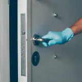 Main tenant, ganté, ouvre une porte voilée.