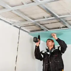 Un ouvrier installe une plaque de plâtre sur une structure métallique pour créer un faux plafond placo.