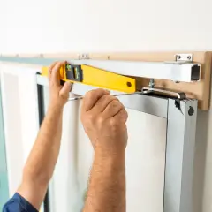 Pose en applique porte : un ouvrier ajuste un rail avec un niveau à bulle et un tournevis pour une installation parfaite.