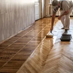 Pose de carrelage imitation parquet : un professionnel applique une couche protectrice sur un sol en chevrons.