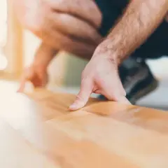Un homme s'accroupit pour faire un plancher bois, posant délicatement une lame de parquet.