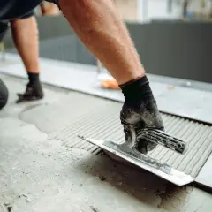 Un carreleur utilise une truelle pour étaler du mortier, un élément essentiel de l'outillage du carreleur, avant de poser une nouvelle dalle.