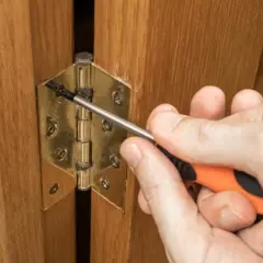 Main tenant une visseuse, une personne ajuste une charnière plate sur une porte en bois.