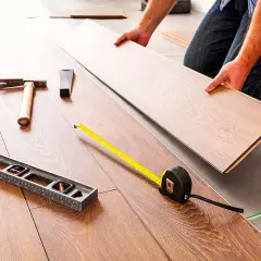 Pose d'un coupe parquet flottant. Outils de pose : niveau, marteau, mètre ruban.