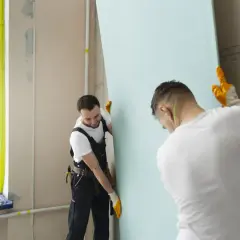 Deux ouvriers installent une plaque de plâtre. Attention à la poussière de plâtre, danger pour les voies respiratoires.