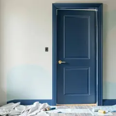 Une porte bleu marine, relookée avec des moulures, est prête pour une nouvelle vie. Des rouleaux et pinceaux au sol indiquent un projet de décoration en cours.