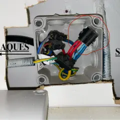 Boîtier électrique ouvert avec fils rouges, bleus et jaunes. Une prise male pour four est visible, connectée à des fils.