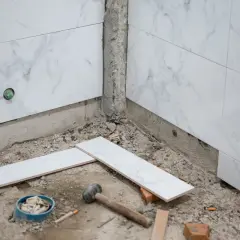 Travaux de salle de bain : pose de carreaux sur du carrelage existant. Marteau, briques et carreaux blancs sont prêts pour le chantier.