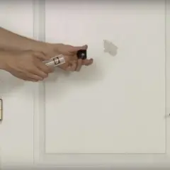 Un homme montre comment réparer un trou dans une porte avec un kit de réparation.