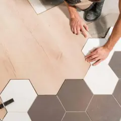 Pose d'un parquet en bois clair à la jonction avec un carrelage hexagonal gris et blanc.