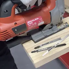 Un bricoleur utilise une scie sauteuse, un type de scie, pour travailler du bois. Trois lames de scie sont visibles.