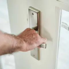 Main d'homme saisissant la poignée d'une porte blanche, prête à en modifier le sens d'ouverture.