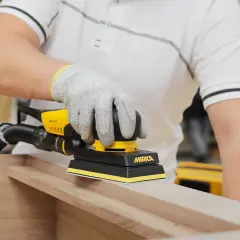 Un artisan utilise une ponceuse pour porte en bois, préparant une surface lisse pour un projet de menuiserie.