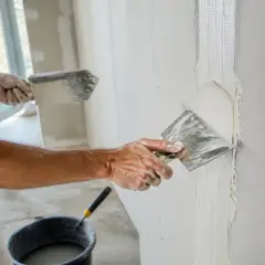 Un ouvrier applique de l'enduit sur une bande de placo. La question "faut-il humidifier les bandes placo" est au cœur de cette étape de finition.