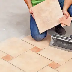 Un carreleur prépare la découpe de carrelage pour un nouveau sol. L'outil de coupe est prêt.