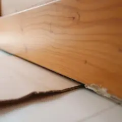 Le bas d'une porte en bois est légèrement surélevé, révélant un espace où du carton est glissé pour le détalonnage.