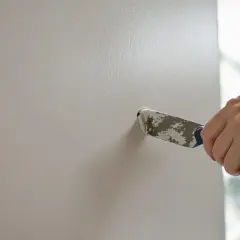 Main tenant, une main utilise un couteau pour réparer un trou dans le mur.
