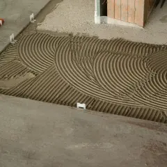 La chape est prête à recevoir les carreaux, avec un mortier étalé en ondulations parfaites. Des croisillons blancs maintiennent l'espacement.