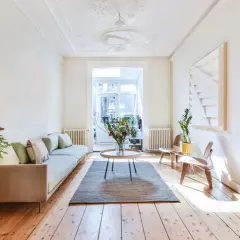 Salon lumineux avec parquet clair, canapé, table basse et bouquet de fleurs. Le parquet semble avoir été traité pour blanchir le bois.