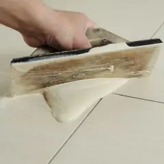 Main tenant utilise une spatule en bois pour faire des joints de carrelage, étalant le mortier sur les carreaux clairs.