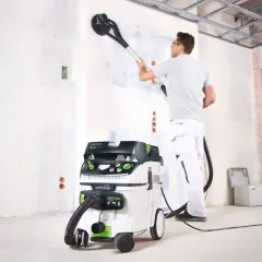 Un ouvrier utilise un aspirateur pour girafe afin de poncer un mur.