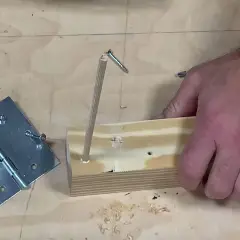 Un bricoleur teste un montage : une vis qui tourne dans le vide, tenue par un bout de bois, à côté d'une charnière.