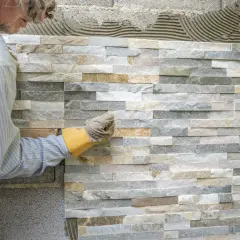 Pose de pierre de parement intérieur, un artisan ajuste une pierre sur un mur en cours de finition.
