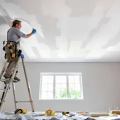 Un peintre sur une échelle pose une toile de verre au plafond.