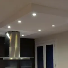 Un caisson plafond avec spots éclaire une cuisine moderne. La hotte en inox et les meubles sombres créent un contraste élégant.