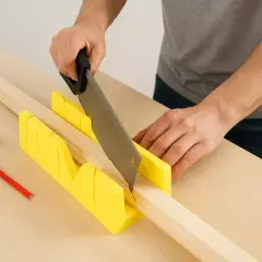 Main tenant une scie pour réaliser une coupe à onglet précise dans une pièce de bois. Un mètre ruban et un crayon sont à proximité.