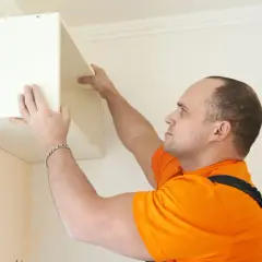 Un homme en t-shirt orange est en train de fixer un caisson blanc au mur.