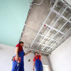 Deux ouvriers installent une structure métallique pour un schema montage placo plafond. Des fils électriques sont déjà en place.