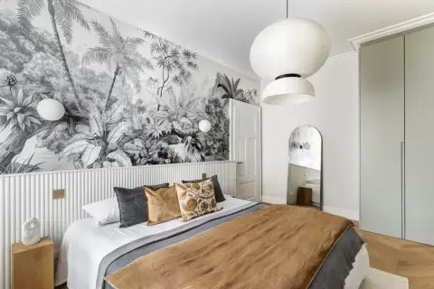 Une chambre avec une tête de lit en papier peint jungle. Le papier peint noir et blanc crée une ambiance tropicale.