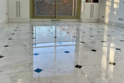 Sol en marbre blanc poli, orné de carreaux noirs, reflétant la lumière. Une rénovation marbre réussie qui illumine la pièce.
