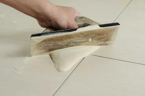Main tenant utilise une spatule en bois pour faire des joints de carrelage, étalant le mortier sur les carreaux clairs.