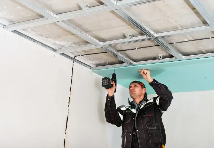 Un ouvrier installe une plaque de plâtre sur une structure métallique pour créer un faux plafond placo.