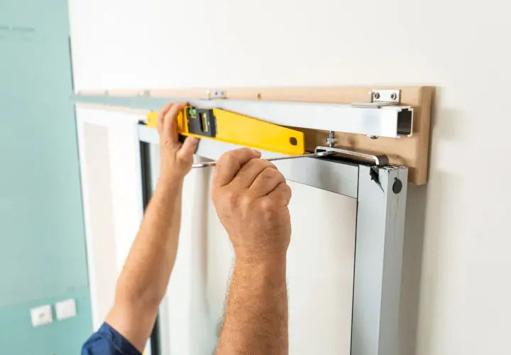 Pose en applique porte : un ouvrier ajuste un rail avec un niveau à bulle et un tournevis pour une installation parfaite.