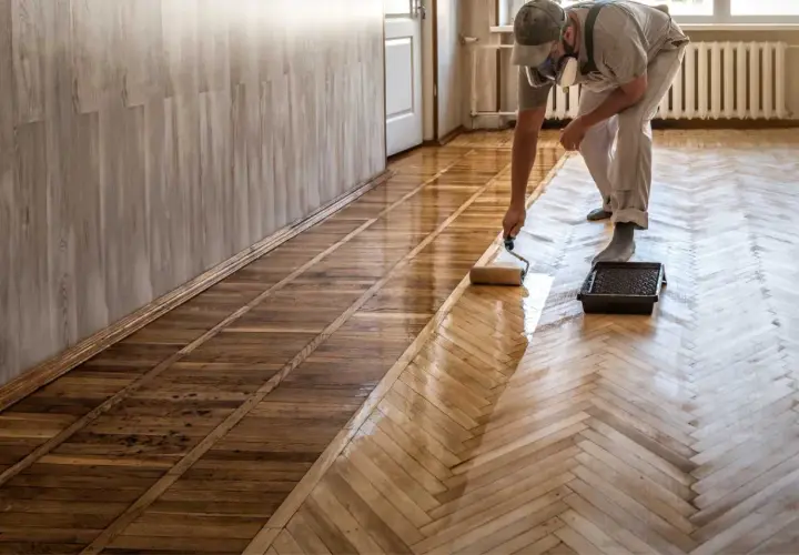 Pose de carrelage imitation parquet : un professionnel applique une couche protectrice sur un sol en chevrons.