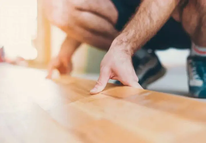 Un homme s'accroupit pour faire un plancher bois, posant délicatement une lame de parquet.