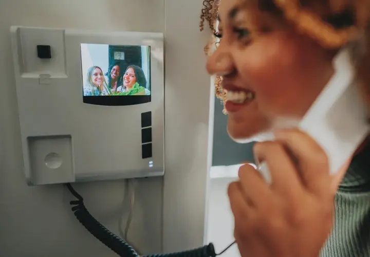 Une femme souriante utilise un visiophone pour parler à des amies. L'installation du visiophone est simple et moderne.