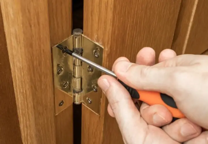 Main tenant une visseuse, une personne ajuste une charnière plate sur une porte en bois.