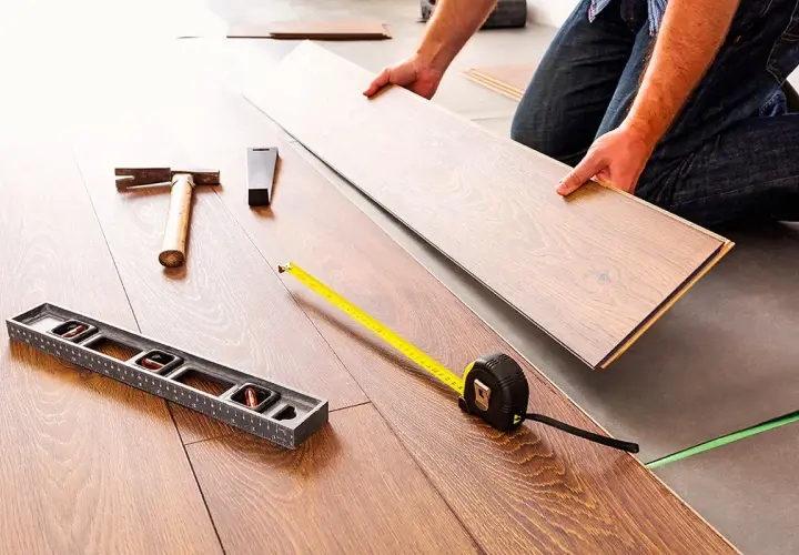 Pose d'un coupe parquet flottant. Outils de pose : niveau, marteau, mètre ruban.