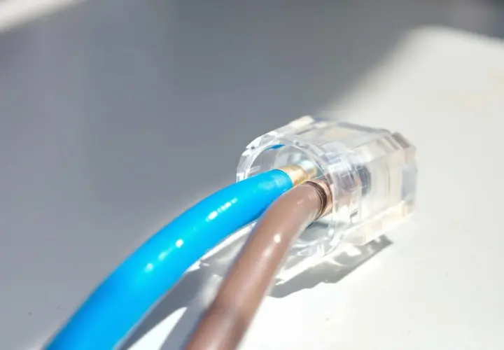 Connexion électrique sécurisée : deux fils, un bleu et un marron, sont raccordés sans domino dans un connecteur transparent.