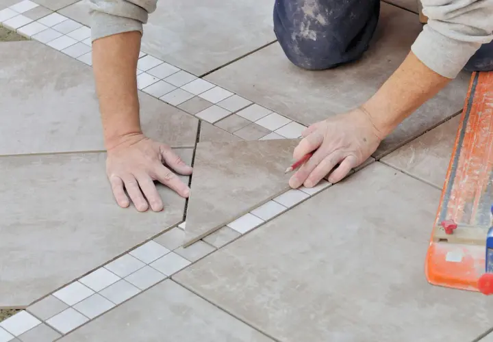 Mains expertes en pose carrelage, ajustant une pièce avec précision. Un coupe-carreau orange est visible.