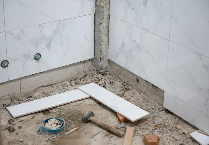 Travaux de salle de bain : pose de carreaux sur du carrelage existant. Marteau, briques et carreaux blancs sont prêts pour le chantier.