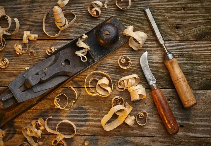 Un rabot, un ciseau et un couteau à bois, outils pour travailler le bois à la main, entourés de copeaux sur un établi rustique.