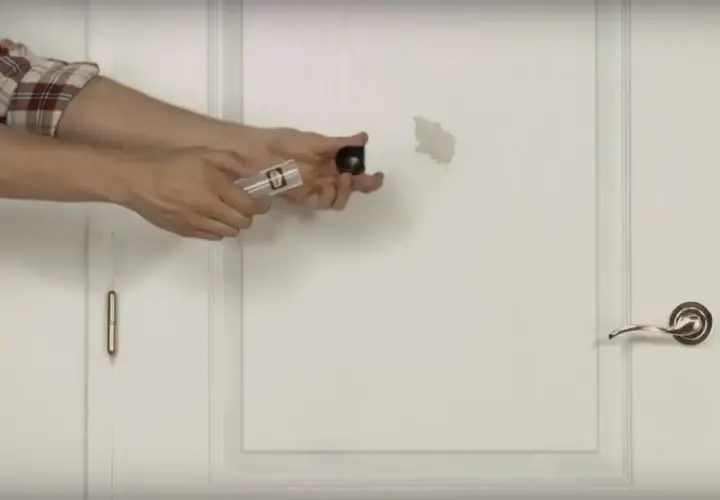 Un homme montre comment réparer un trou dans une porte avec un kit de réparation.
