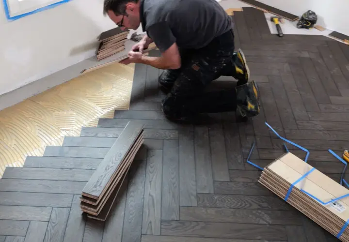 Pose de parquet en pose bâton rompu. Un artisan applique de la colle sur le sol avant de poser les lames de bois.