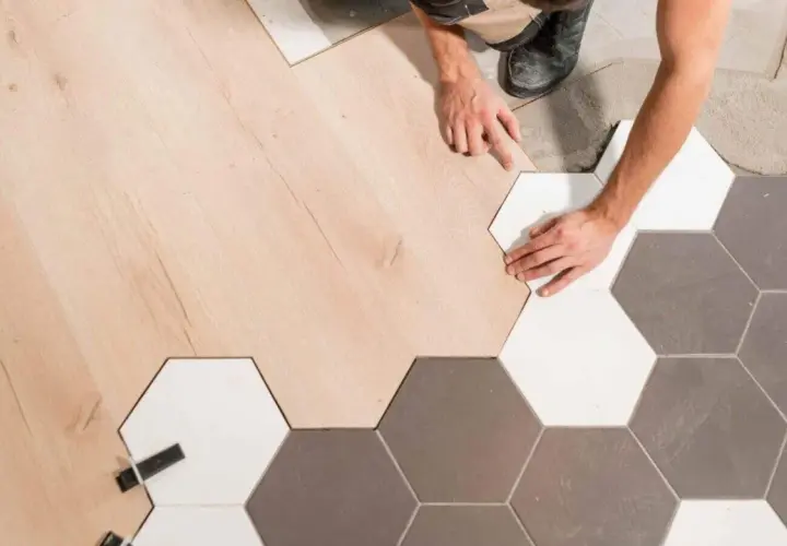 Pose d'un parquet en bois clair à la jonction avec un carrelage hexagonal gris et blanc.