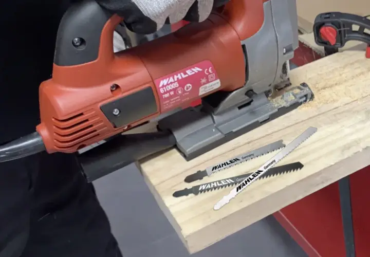 Un bricoleur utilise une scie sauteuse, un type de scie, pour travailler du bois. Trois lames de scie sont visibles.